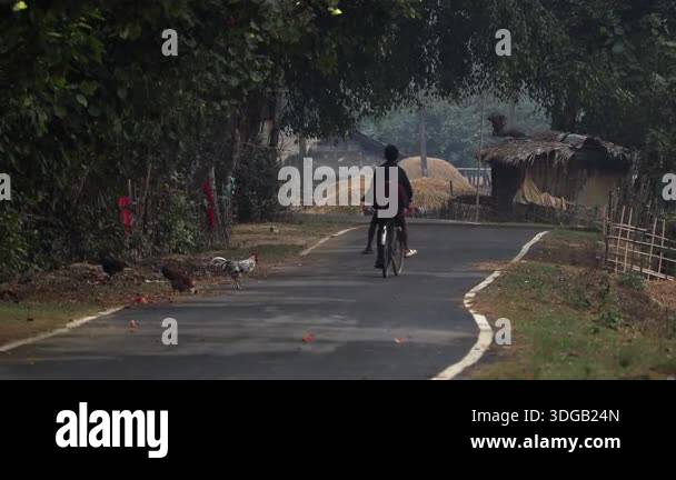 Assam, India January 2026:A person riding a bicycle along a narrow ...
