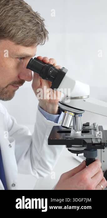 A man scientist carefully observing through a microscope in a brightly ...