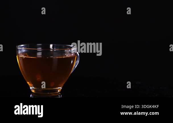 A glass cup filled with tea sits on a black background, highlighting ...