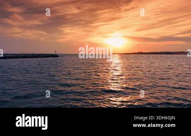 The sun sets over the water, casting orange and yellow light across the ...