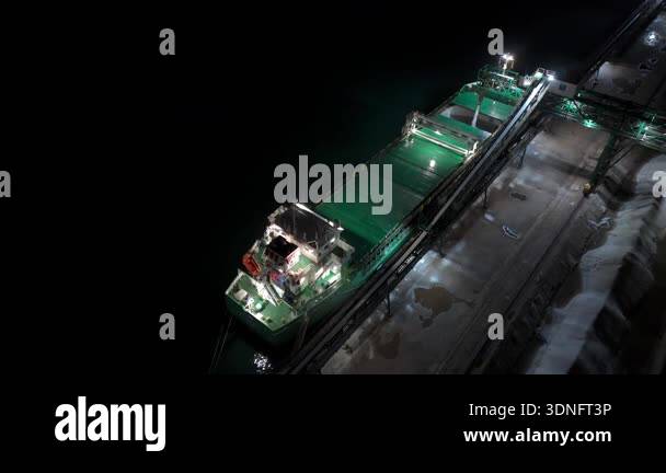 Aerial view of cargo ship loading at industrial port at night ...