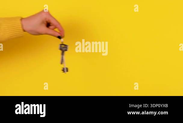 Close-up of a hand holding and jingling house keys on a bright yellow ...