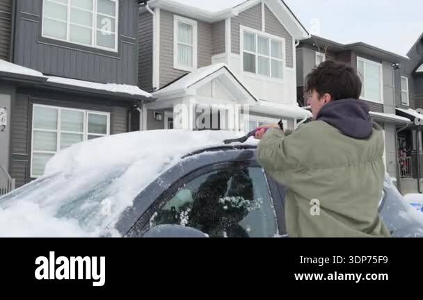 man-removes-accumulated-snow-from-the-car-roof-using-a-brush-in-a