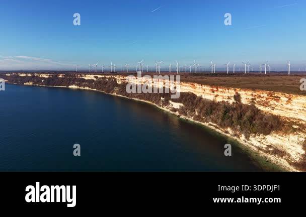 Cliffs rise above the water with green vegetation along the shore. Wind ...