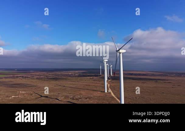 Wind turbines stand tall in a wide field with a blue sky and clouds ...