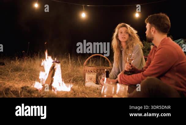 Two people relax by a fire, sipping drinks and having a conversation ...