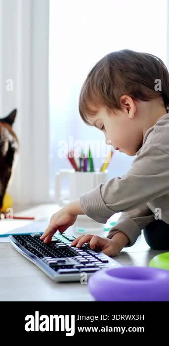 Caucasian toddler playing with computer keyboard. Black cat stands at ...