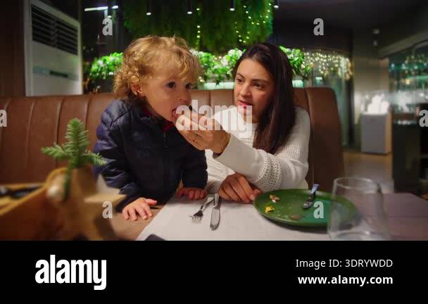 Parent offering bite of food to toddler during restaurant visit ...
