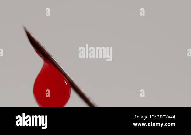 Extreme close-up of a red blood droplet slowly running down the sharp ...