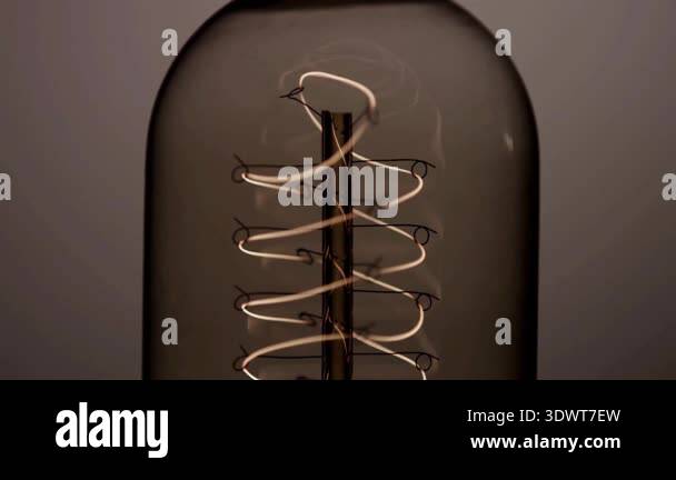 Close up of a vertical spiral filament inside a vintage light bulb as ...