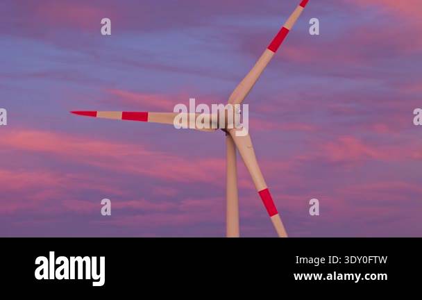 Modern wind turbine stands tall against a dramatic sunset sky with ...