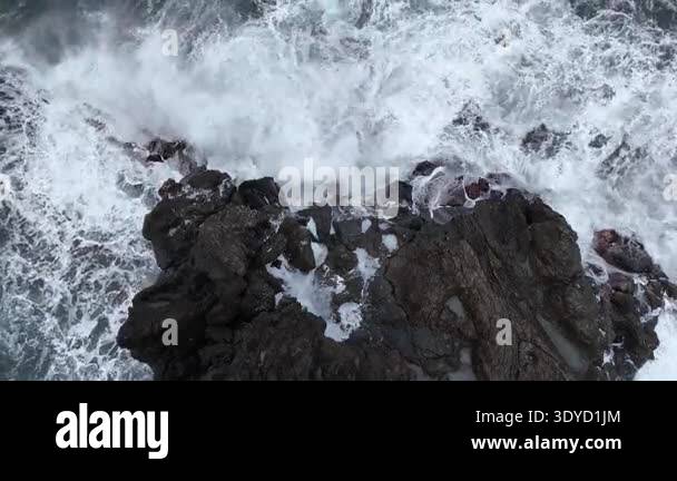 Ocean waves crash against rocky shoreline, creating foam and splashes ...