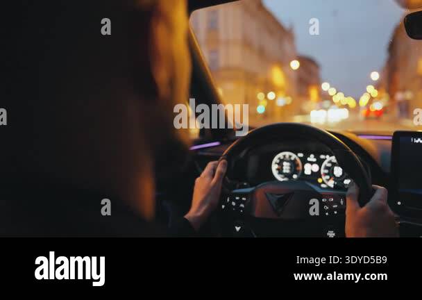 Backseat view on man driving car through bustling city at dusk under ...