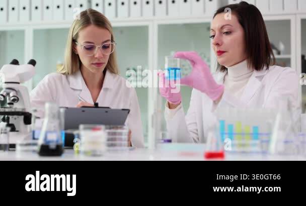 Team scientist makes notes in a report and holds flask with blue liquid ...