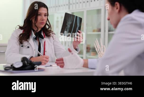 Concentrated female doctor examining X-ray image of hand making notes ...