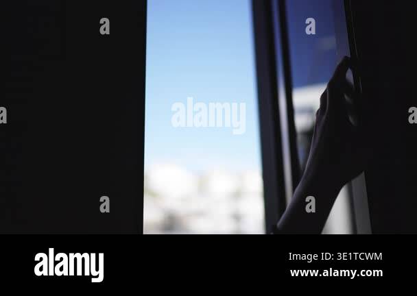 A person hand, silhouetted in a dark room, slides a glass door open and ...