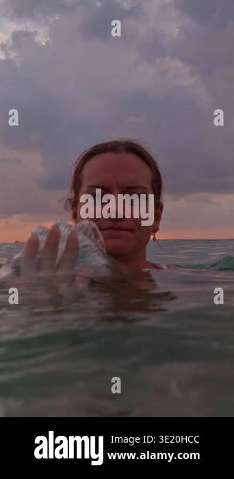 Vertical video. Woman hand pushing sea water toward camera creating ...