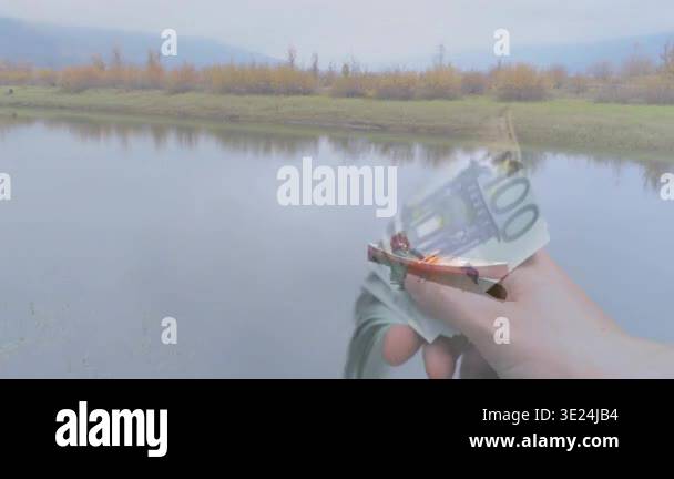 Right hand entering frame, fanning 100 banknotes over lakeshore ...