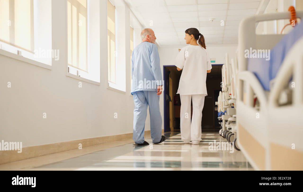 Nurse assisting elderly patient walking down hospital corridor Stock ...