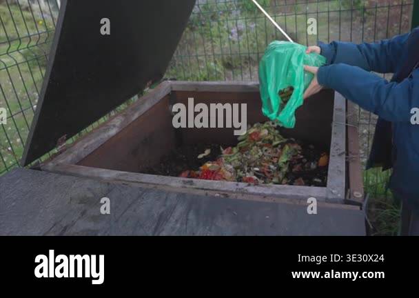 Throwing Compost Man throwing biodegradable kitchen scraps into a wooden compost bin ...