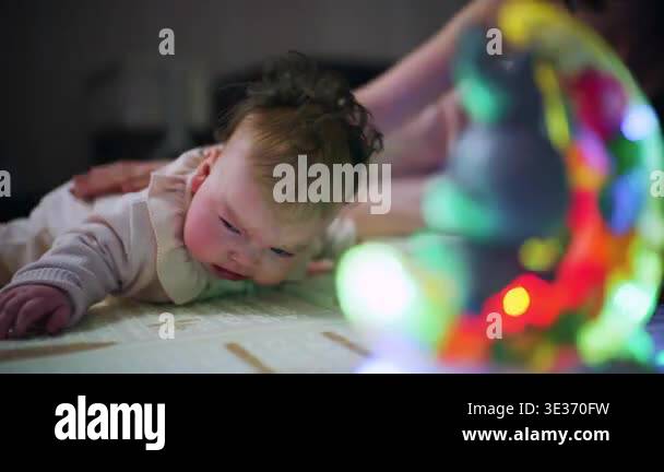 Baby lying on a play mat during tummy time while crying, with caregiver ...