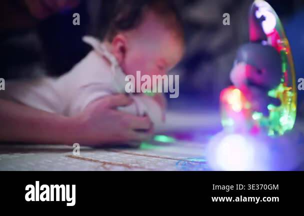 Close up of infant lying on play mat watching a glowing toy with ...
