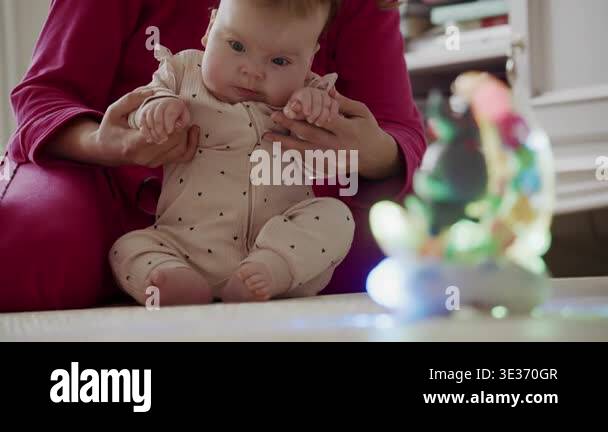 Infant sitting on a play mat while caregiver supports the baby during ...