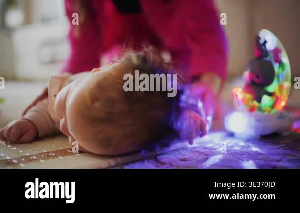 Infant practicing tummy time on a soft play mat while caregiver gently ...