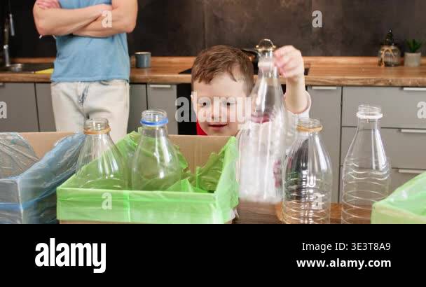 Young boy lifts empty plastic bottle above green recycling box in ...