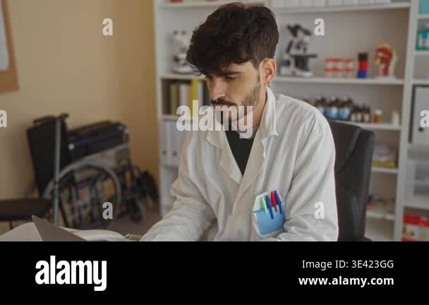 Young man with beard working on laptop in hospital office, wearing ...