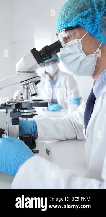 Senior male scientist wearing a protective mask, cap, and gloves ...