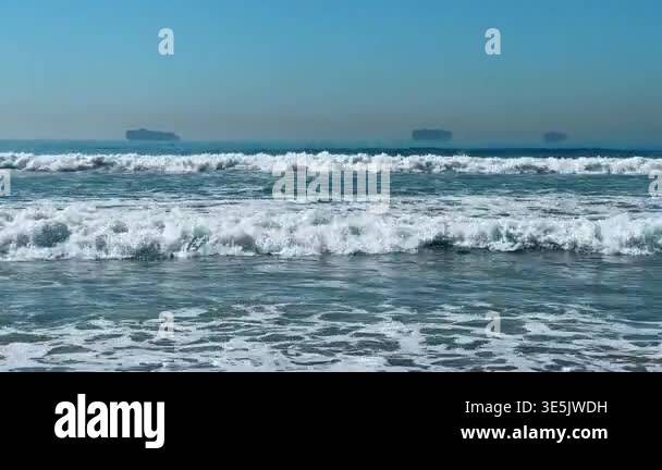 Ocean waves breaking with cargo ships on distant horizon. Foamy white ...