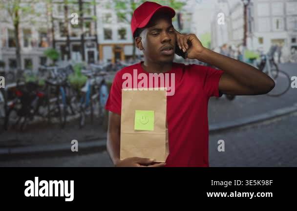 Man wearing red cap and holding paper bag with yellow sticky note and ...