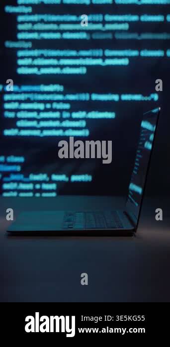 Laptop on dark desk with blue programming code projected in background ...