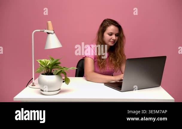 Young female student working on laptop typing on keyboard at white desk ...