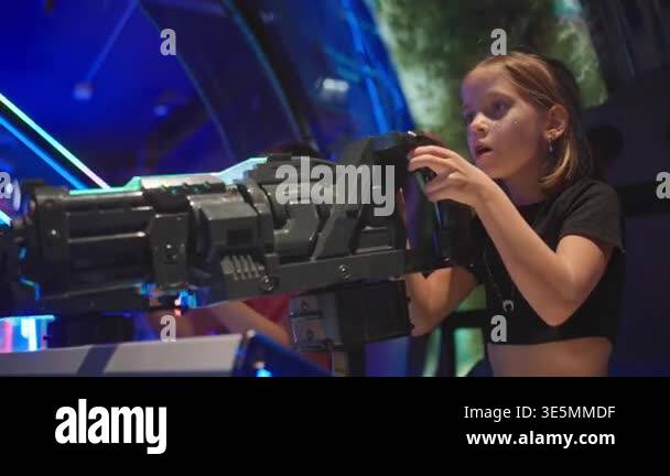 Girl playing on large shooter arcade game, surrounded by glowing lights ...