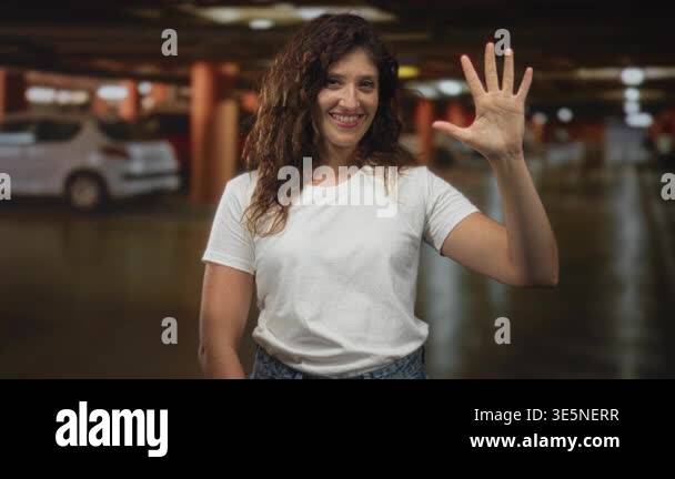 Woman wearing white tshirt holds up open hand beside parked car in ...