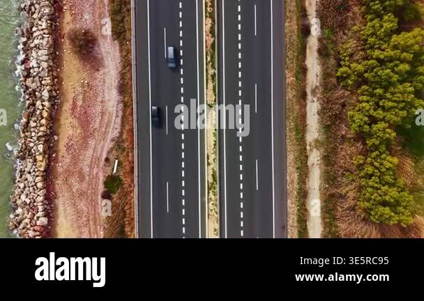 Two cars travel on a highway that runs parallel to a beach, separating ...