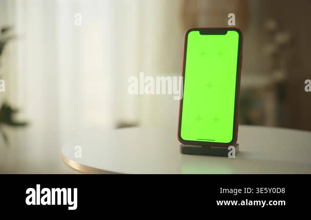Modern smartphone standing on a dock with a green chroma key screen ...