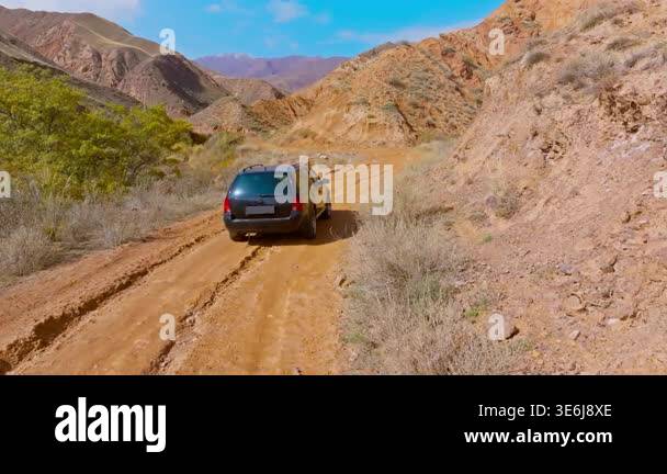 Car navigates a dirt road through eroded sandstone mountains in ...