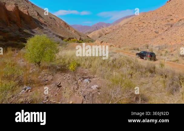 Black car navigates rugged dirt road through dry, mountainous canyon ...