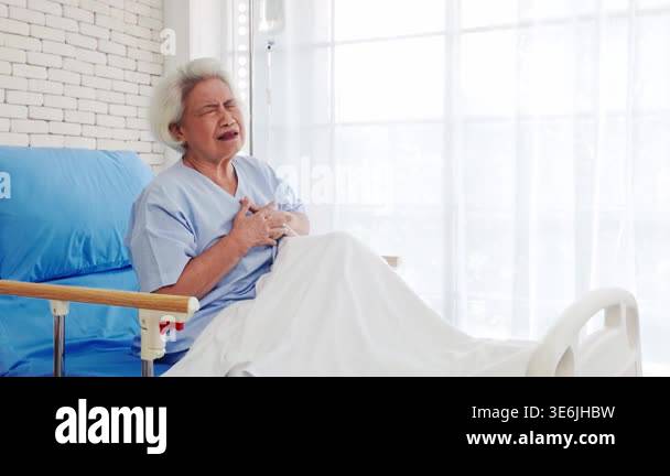 An elderly woman in a hospital bed clutches her chest in visible pain ...