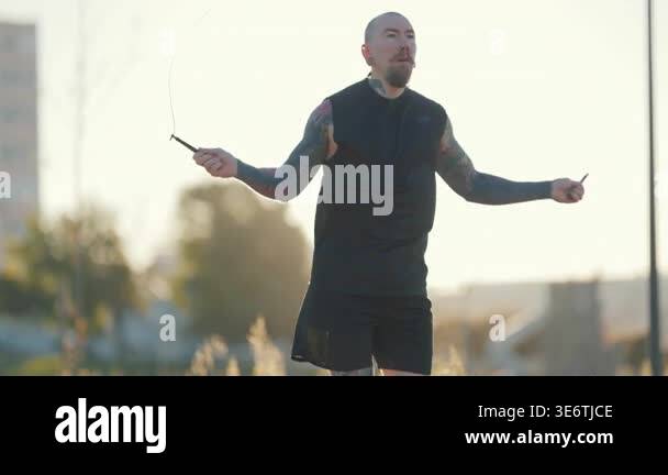 Young athletic man with tattoos working out with a jump rope outdoors ...