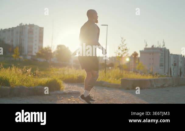 Athletic man with tattoos training with a jump rope in an urban park at ...