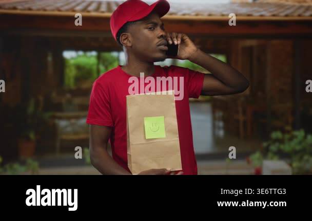 Young man in red cap holds parcel and holds smartphone to ear at ...