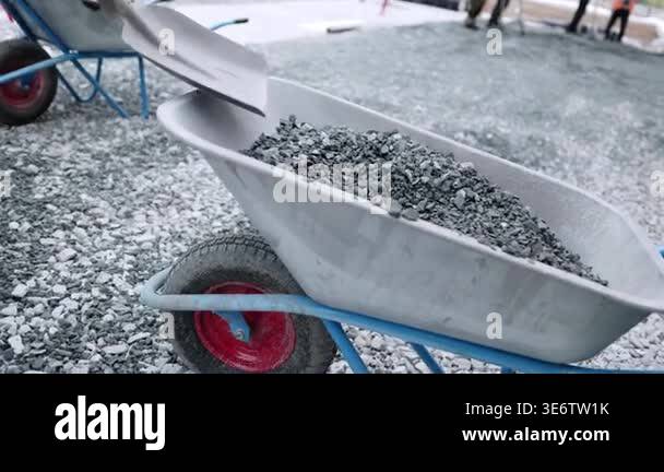 Builder in uniform takes gravel from wheelbarrow at construction site ...