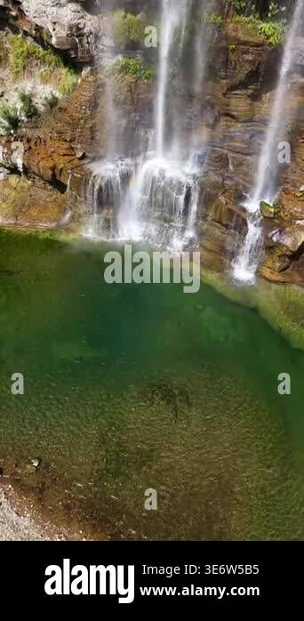 Aerial view of waterfall flowing into deep green pool. Rocks and trees ...