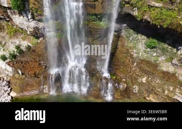 Aerial view of waterfall flowing into deep green pool. Rocks and trees ...