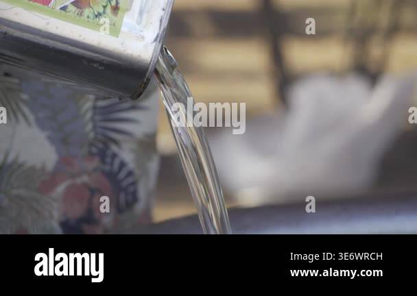 Metal container pouring clear liquid into a bowl on a wooden surface ...