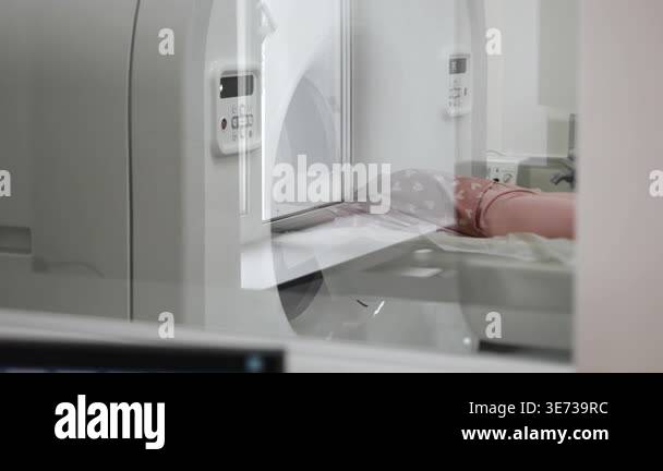 Child undergoing CT scan viewed through glass window from control room ...